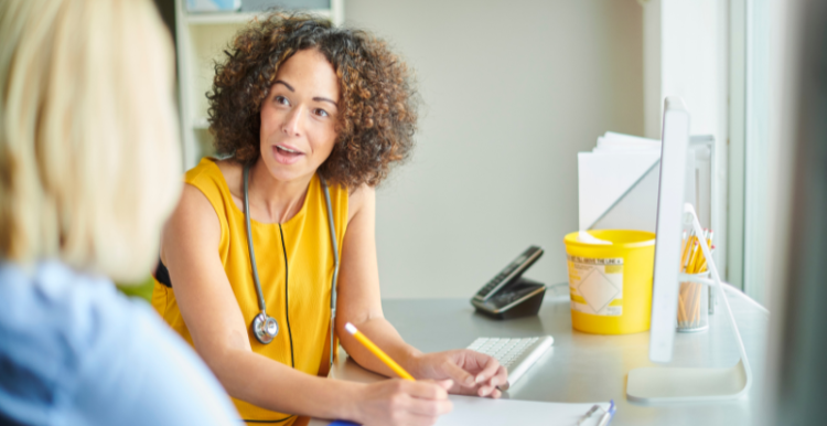 GP wearing a yellow top talking to a patient in the foreground