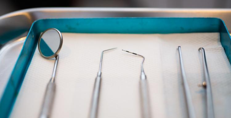 A close up photo of several dentist's tools, including dental probes and a mouth mirror, laid out next to each other.
