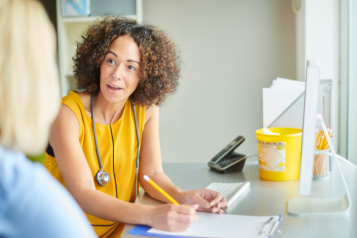 GP wearing a yellow top talking to a patient in the foreground