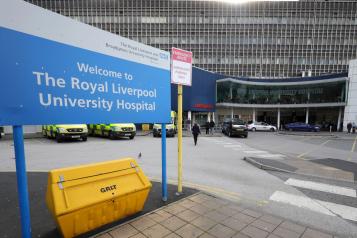 A sign reading 'The Royal Liverpool University Hospital'. In the background is the entrance to the A&E department at the Royal, with ambulances parked outside.