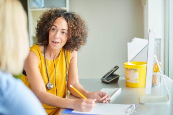 GP wearing a yellow top talking to a patient in the foreground