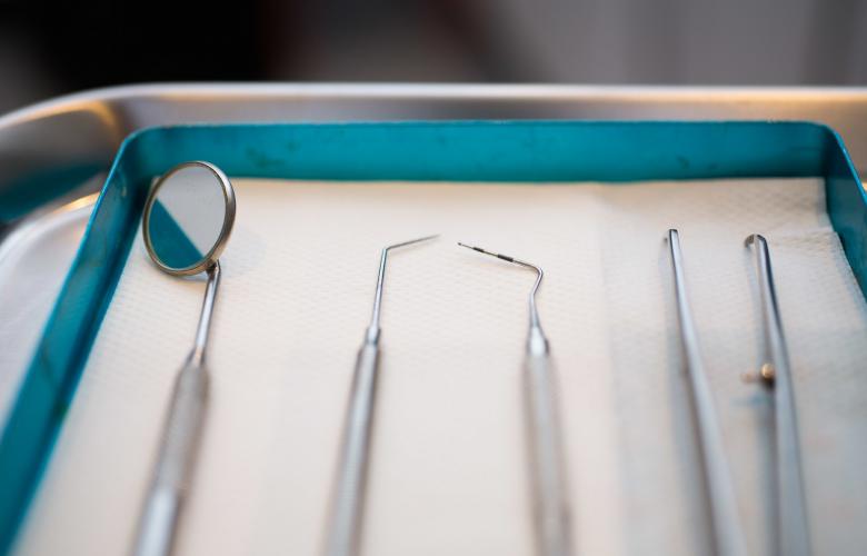 A close up photo of several dentist's tools, including dental probes and a mouth mirror, laid out next to each other.